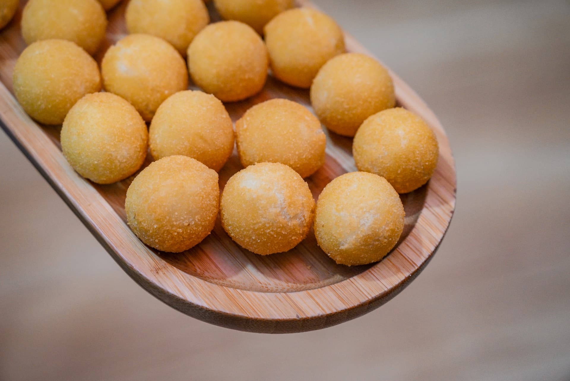 Bolinhos fritos dourados servidos em tábua de madeira na By Ange